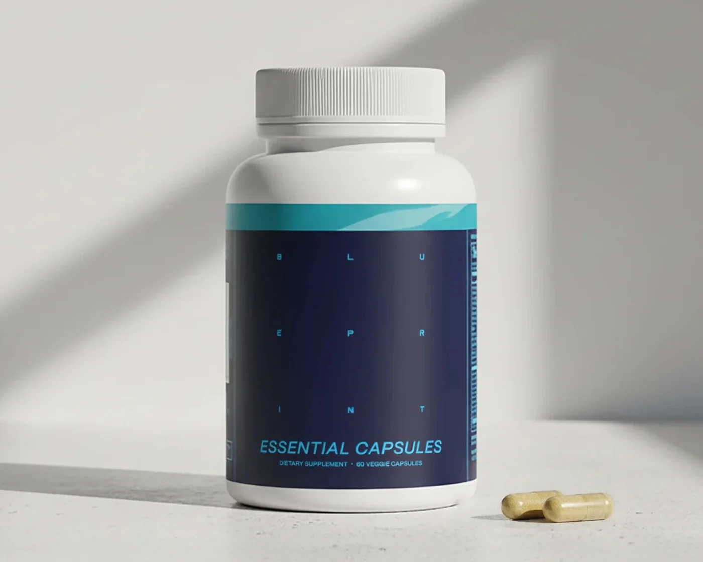 Dose Blueprint Essential Capsules mit zwei Kapseln davor, vor hellem Hintergrund